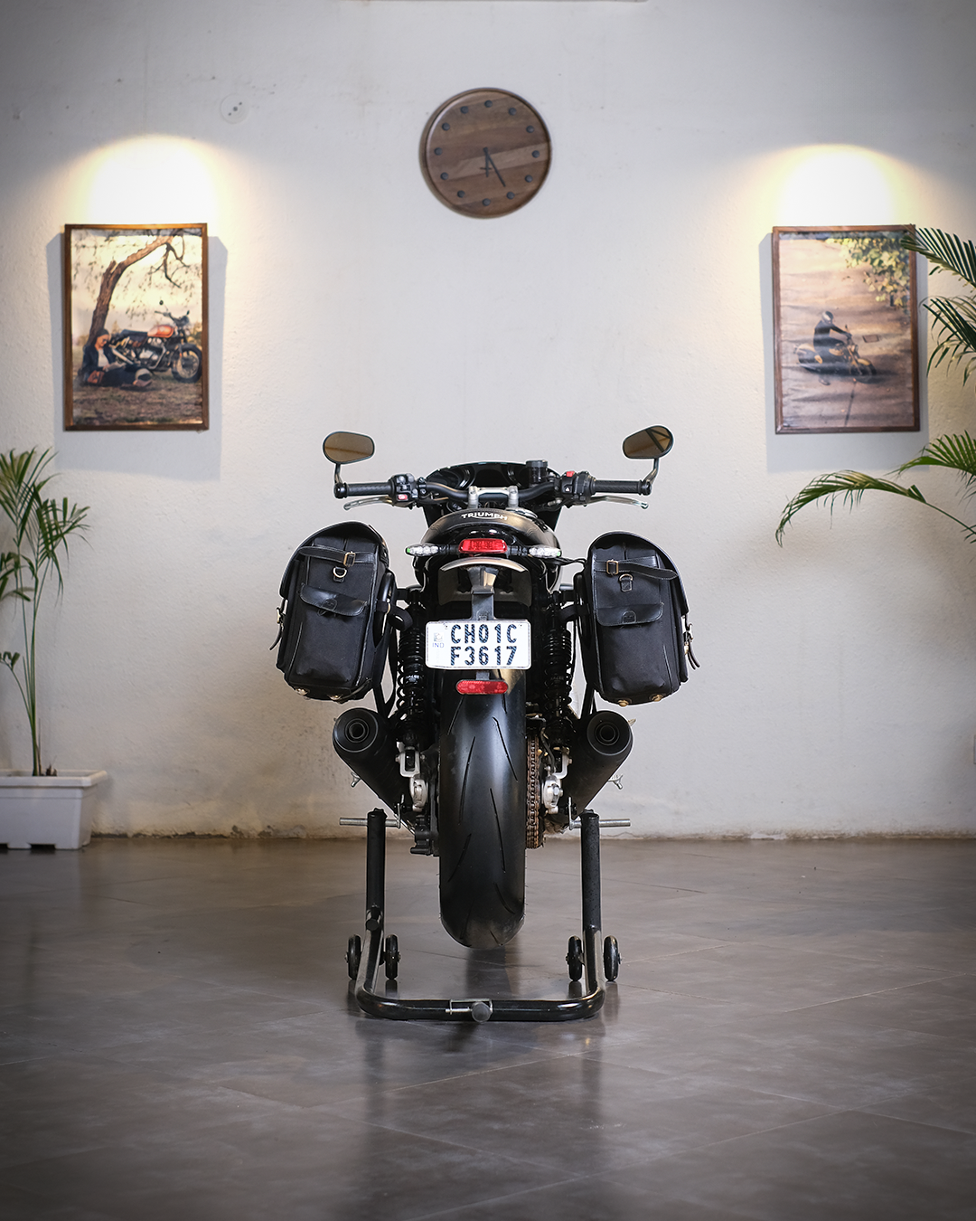 Motorcycle with luggage on a stand in a room with framed pictures and a clock on the wall.
