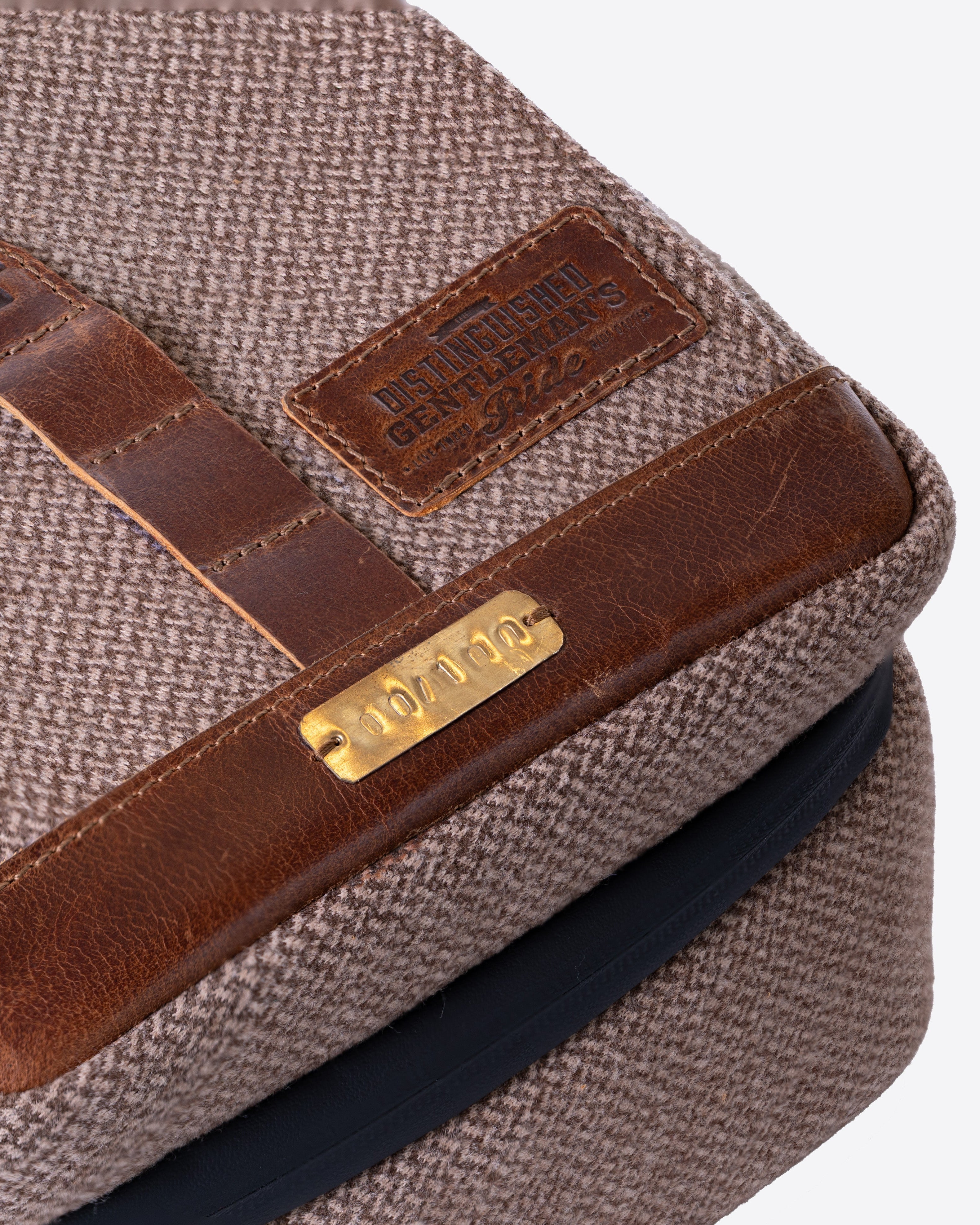 Close-up of a brown leather strap with a gold tag on a textured surface