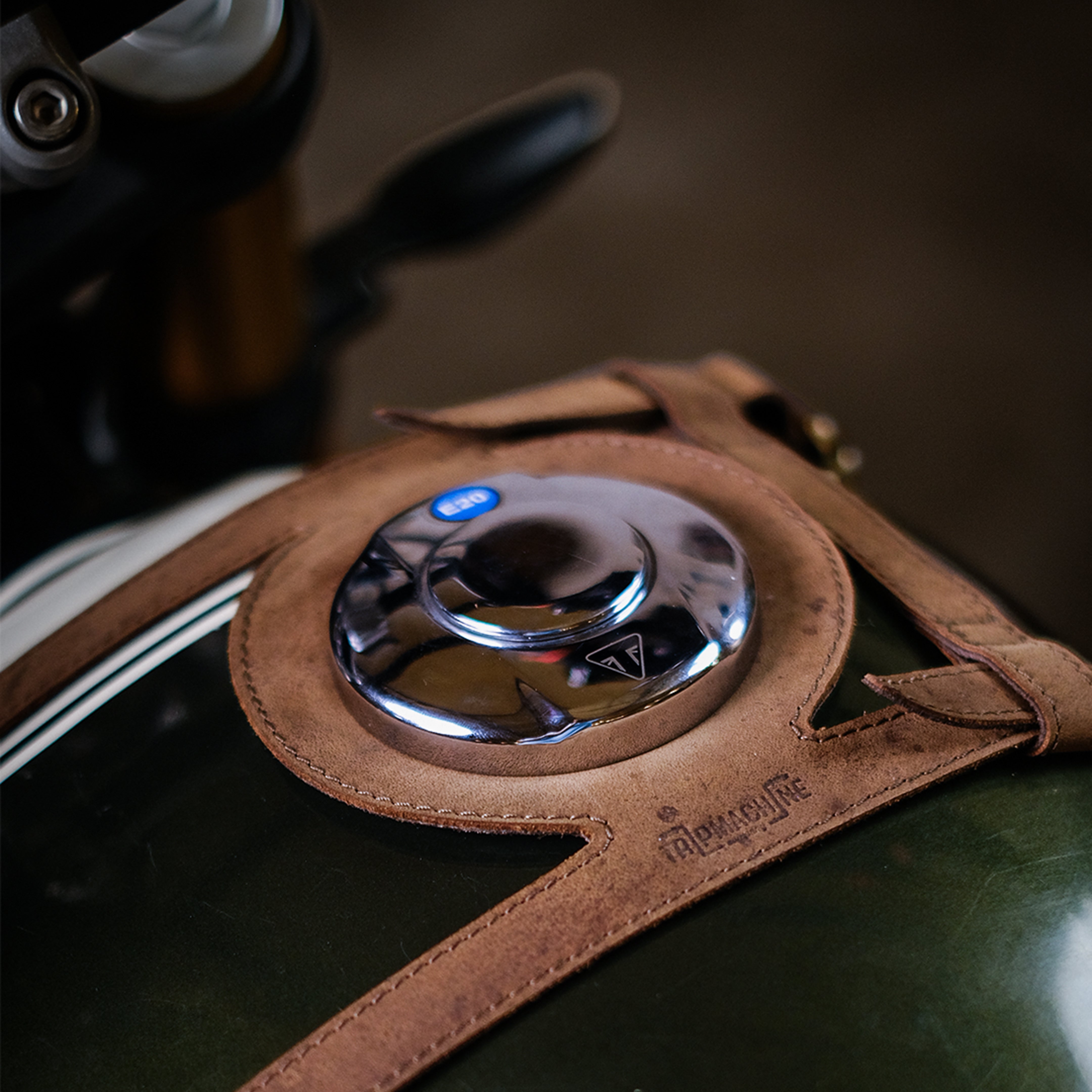 Close-up of a motorcycle fuel tank strap with leather cover and chrome cap.