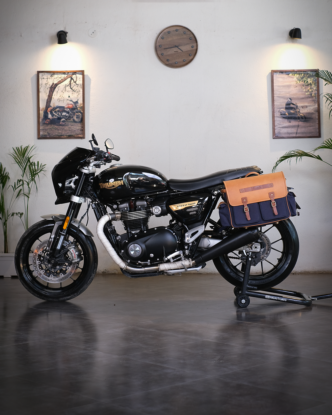 Black motorcycle with a saddlebag in a room with plants and framed pictures on the wall.