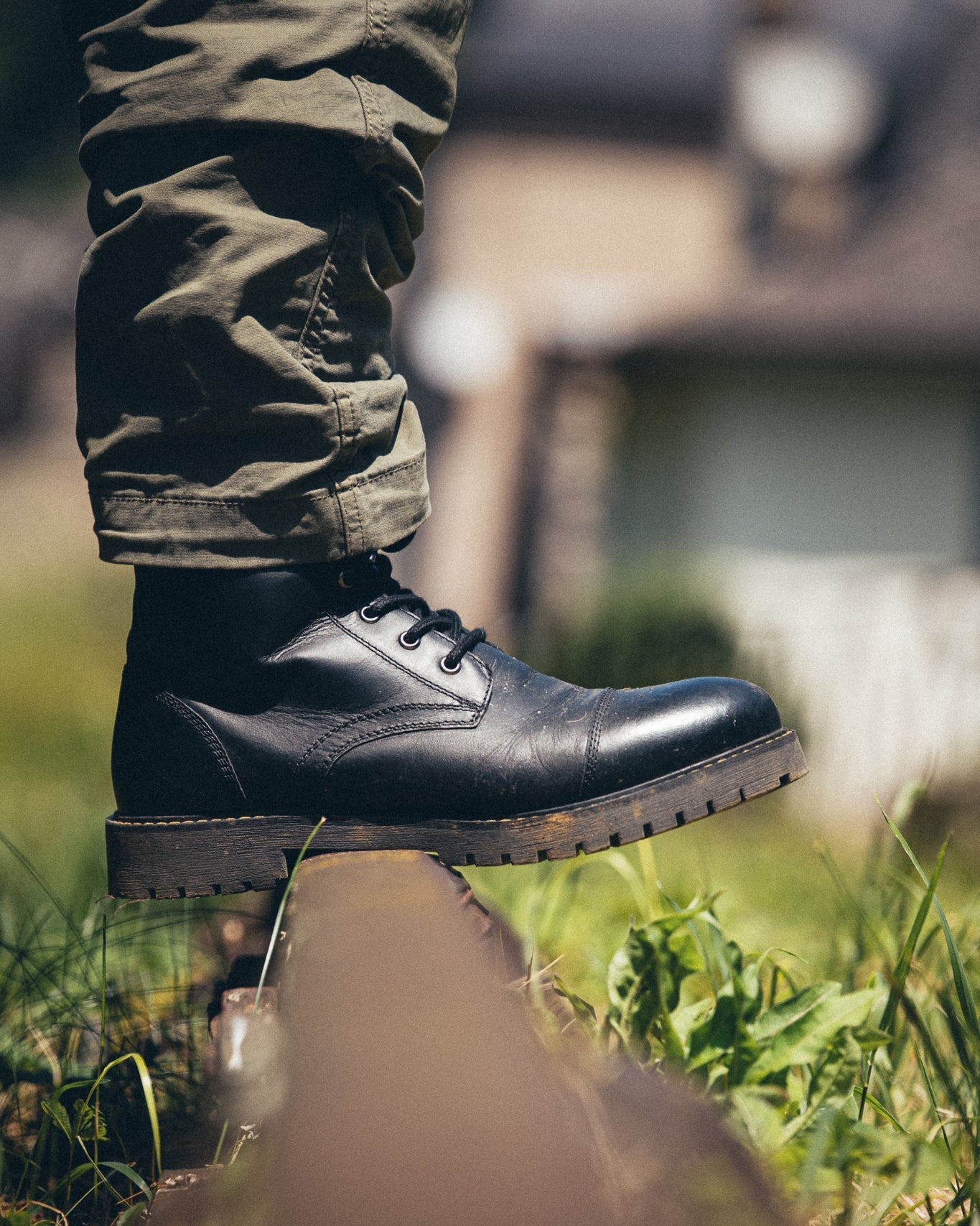 Person wearing black boots and green camouflage pants standing on grass.