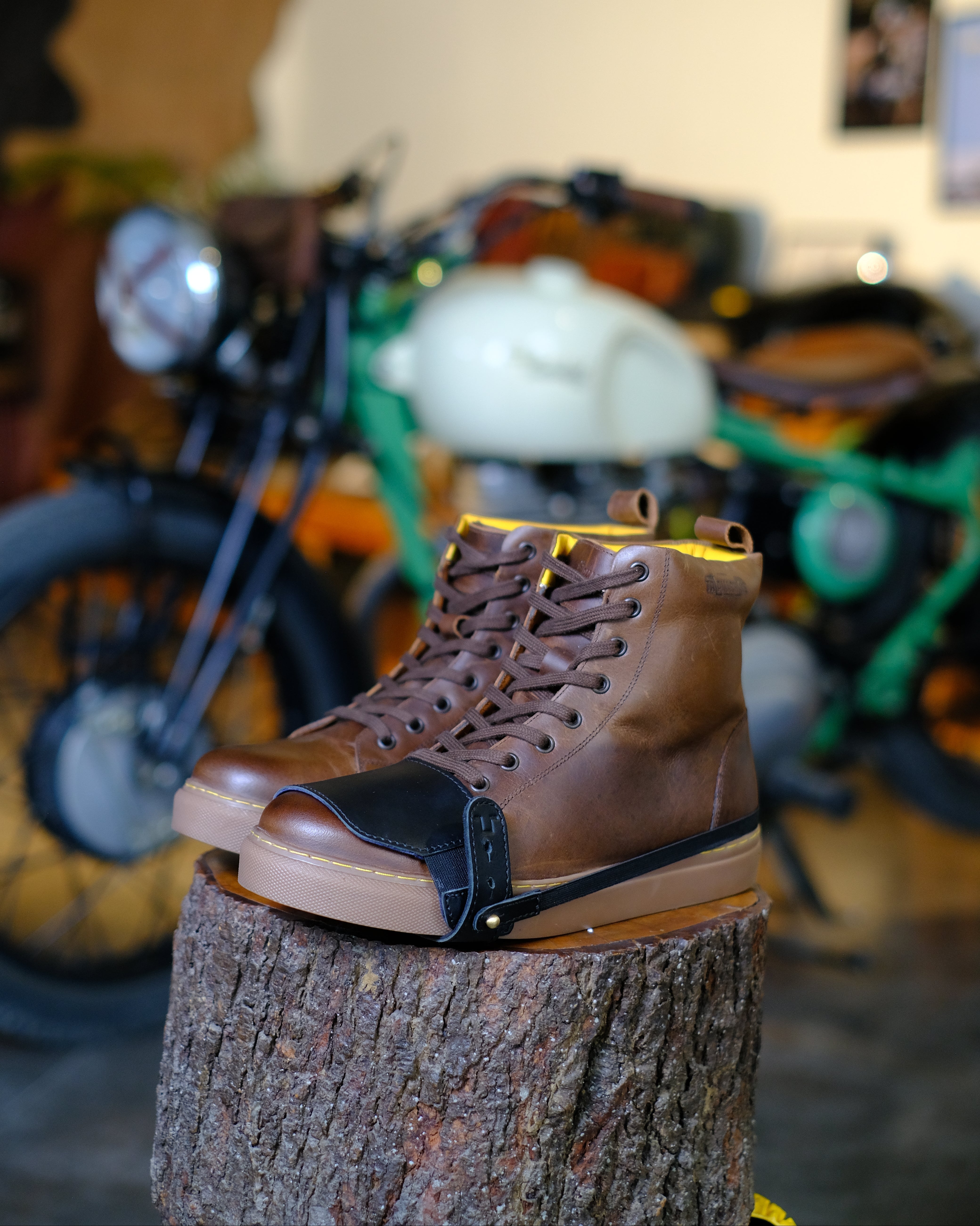 Brown leather boots with black shoe protector on a tree stump with motorcycles in the background