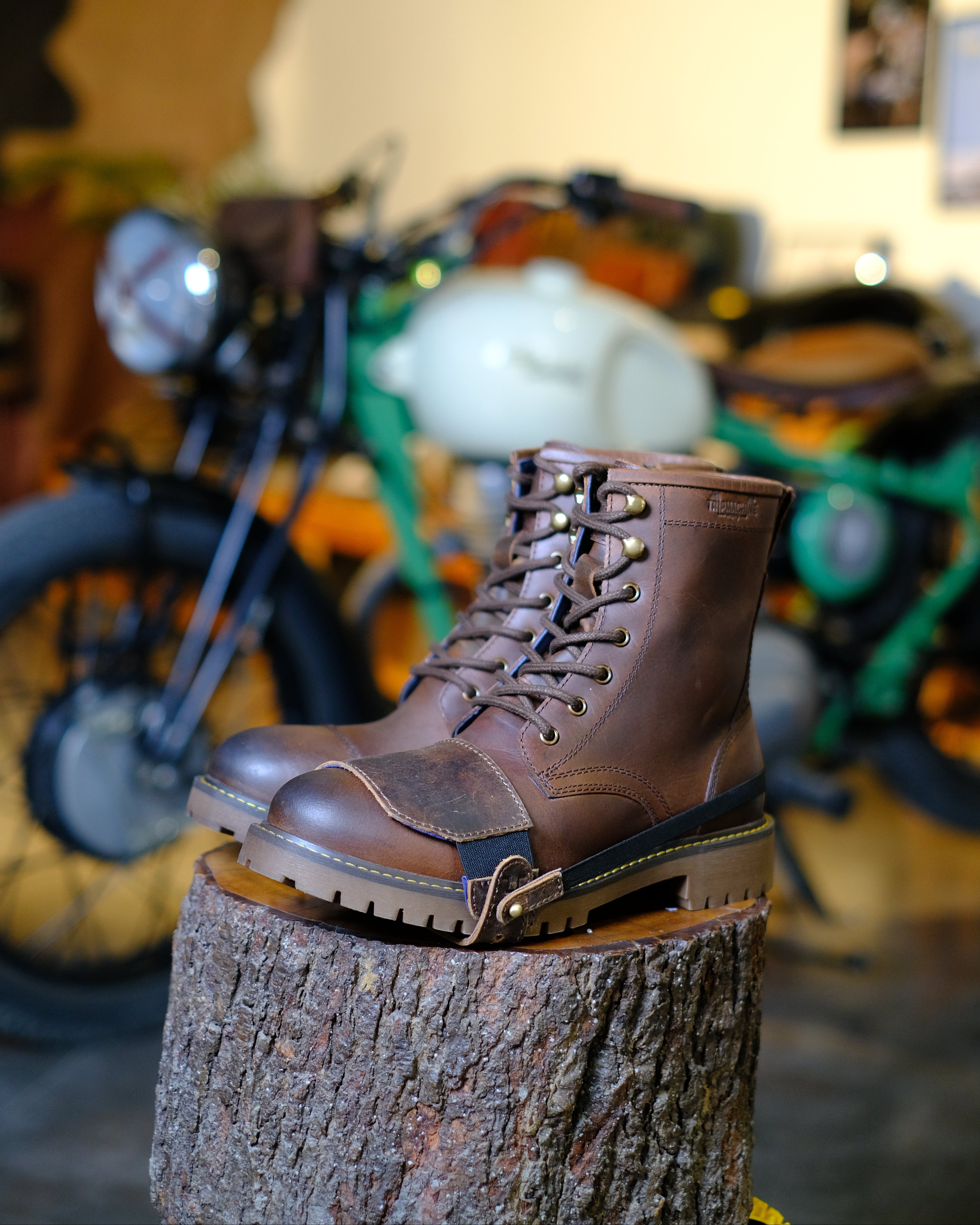 Brown leather boots with mocha shoe protector on a tree stump with a motorcycle in the background