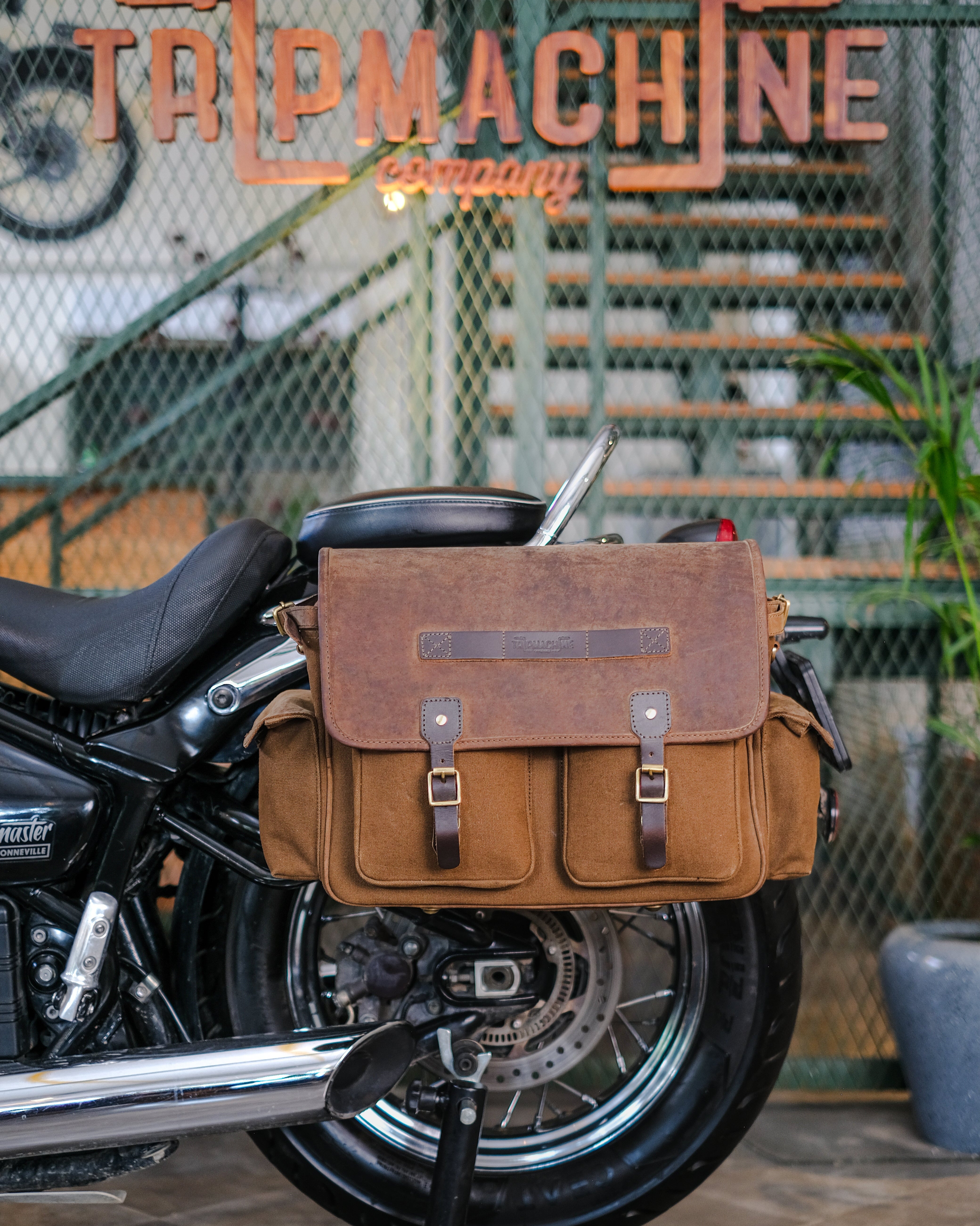 Brown leather bag on a motorcycle with 'Tail Machine Company' sign in the background
