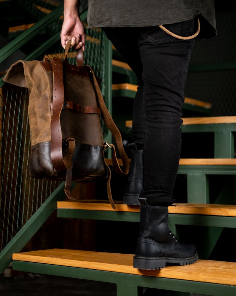 Man on stairs with a brown backpack and black color handmade genuine leather derby boots with ankle, toe and heel protector for bikers