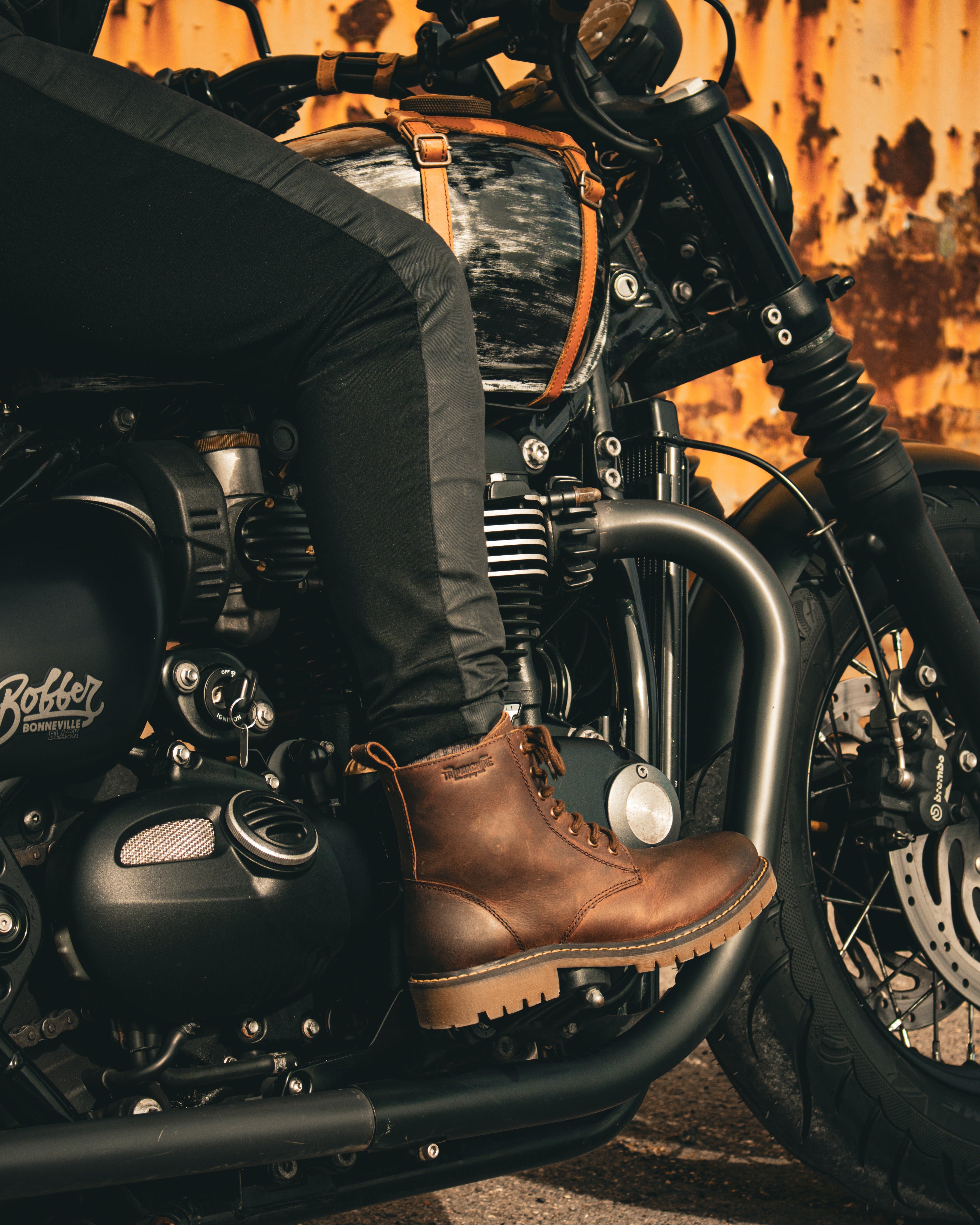 Person wearing brown boots sitting on a motorcycle with a rustic wall background