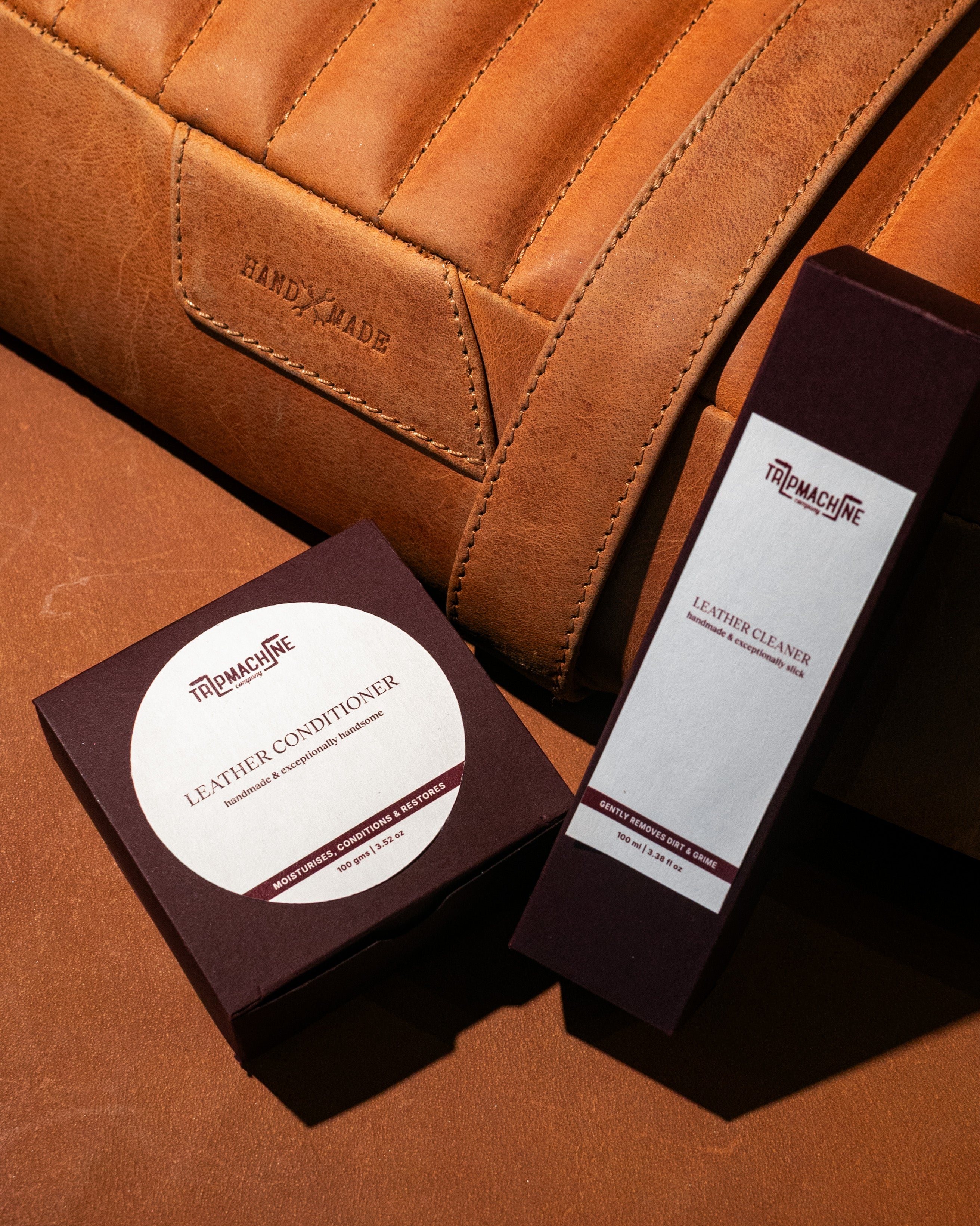Two leather care products on a brown leather surface with 'Handmade' branding.