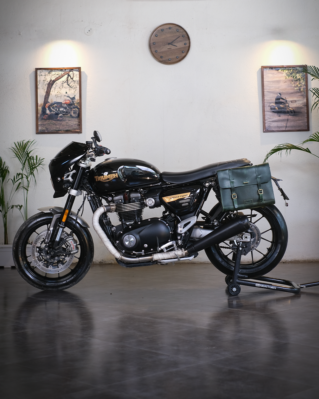 Black motorcycle with green bag in a room with plants and wall art