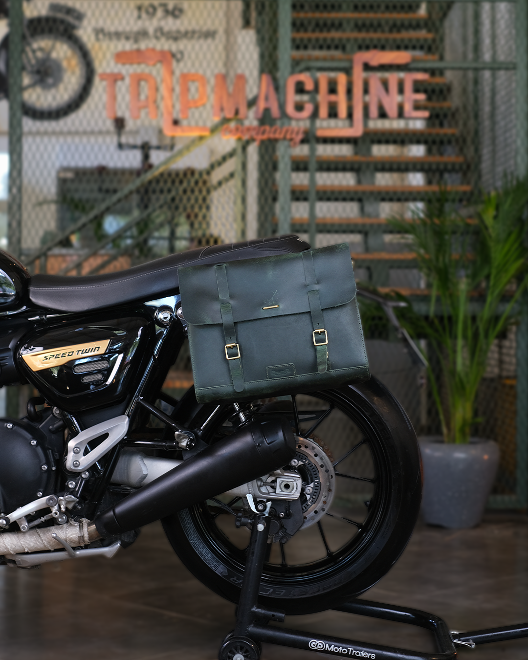 Motorcycle with a green saddlebag in front of a 'Tripmachine' sign.