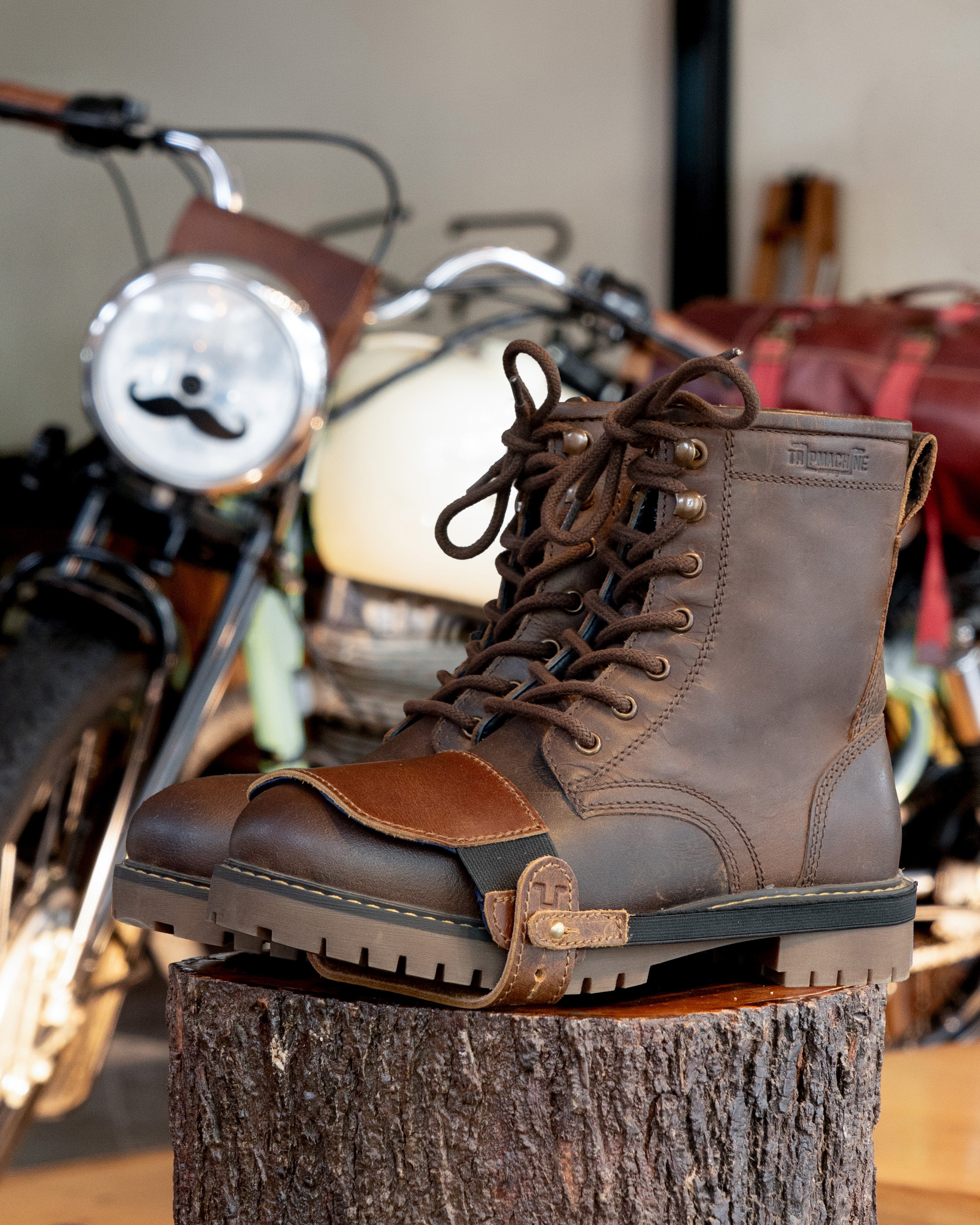 Brown leather boot on a wooden block with a motorcycle in the background