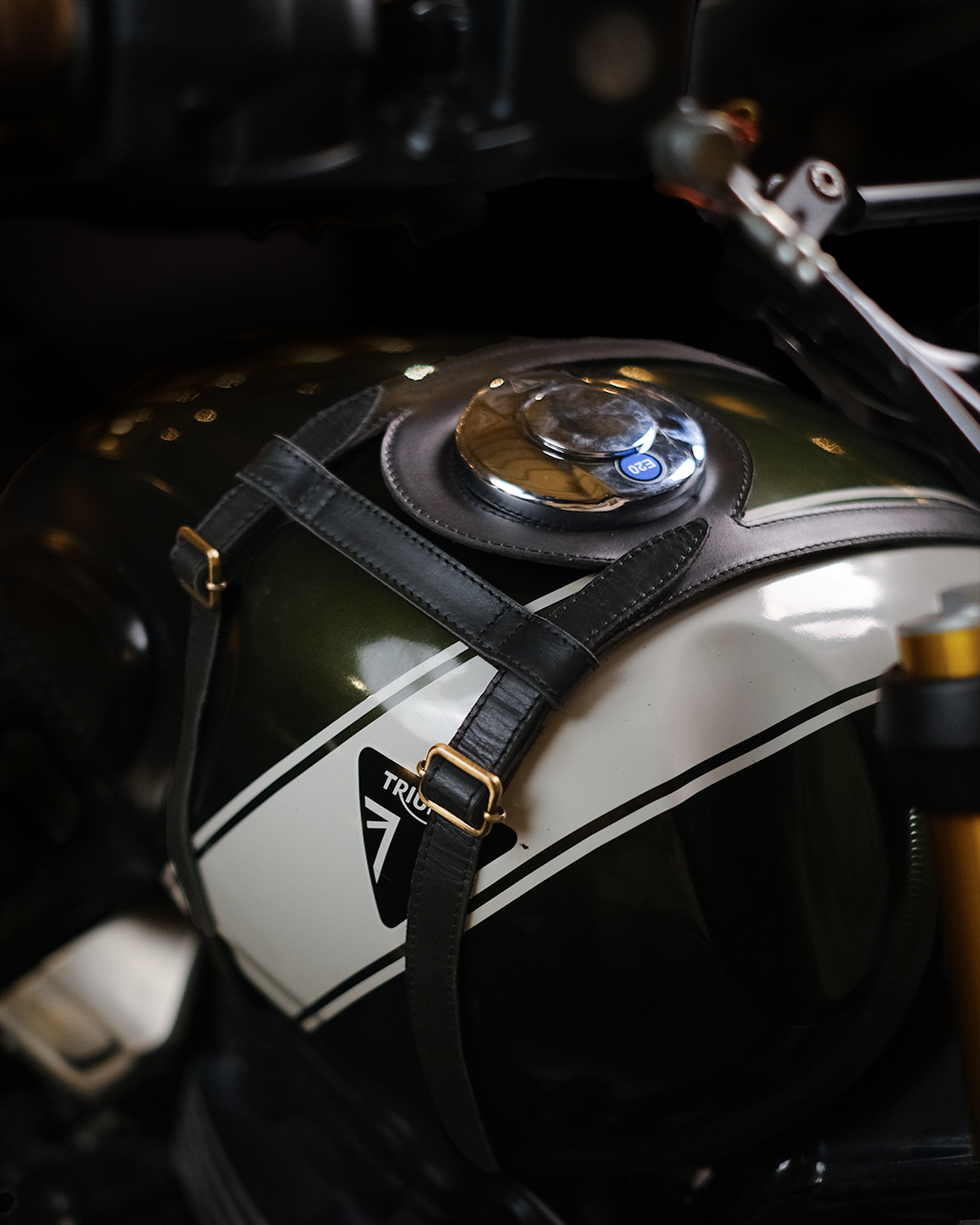 Close-up of a motorcycle fuel tank with a helmet strap and 'Triumph' logo.