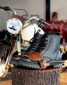 Black leather boots with cognac shoe protector on a wooden block in front of a motorcycle.