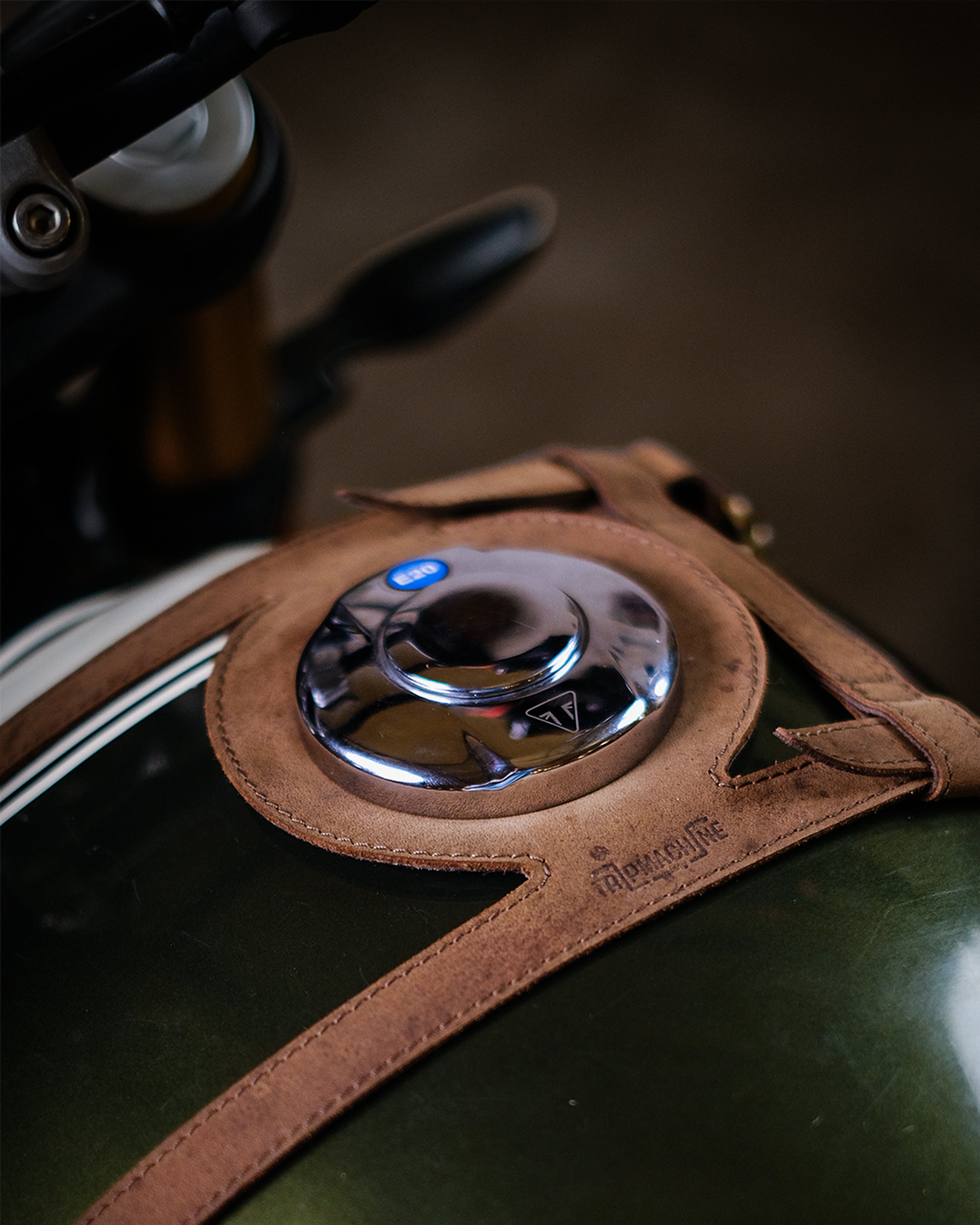 Close-up of a motorcycle fuel tank strap with leather cover and chrome cap.