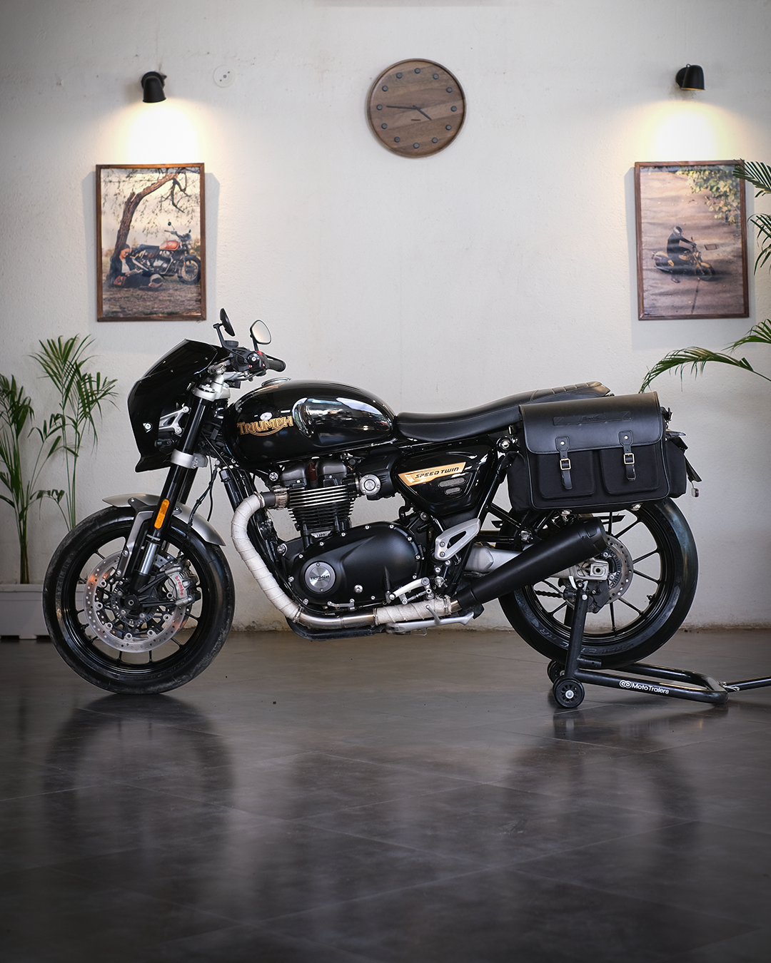 Black motorcycle with saddlebags in a room with plants and framed pictures on the wall.