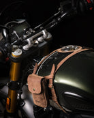 Close-up of a motorcycle with a brown leather pouch with tank strap attached to the fuel tank.