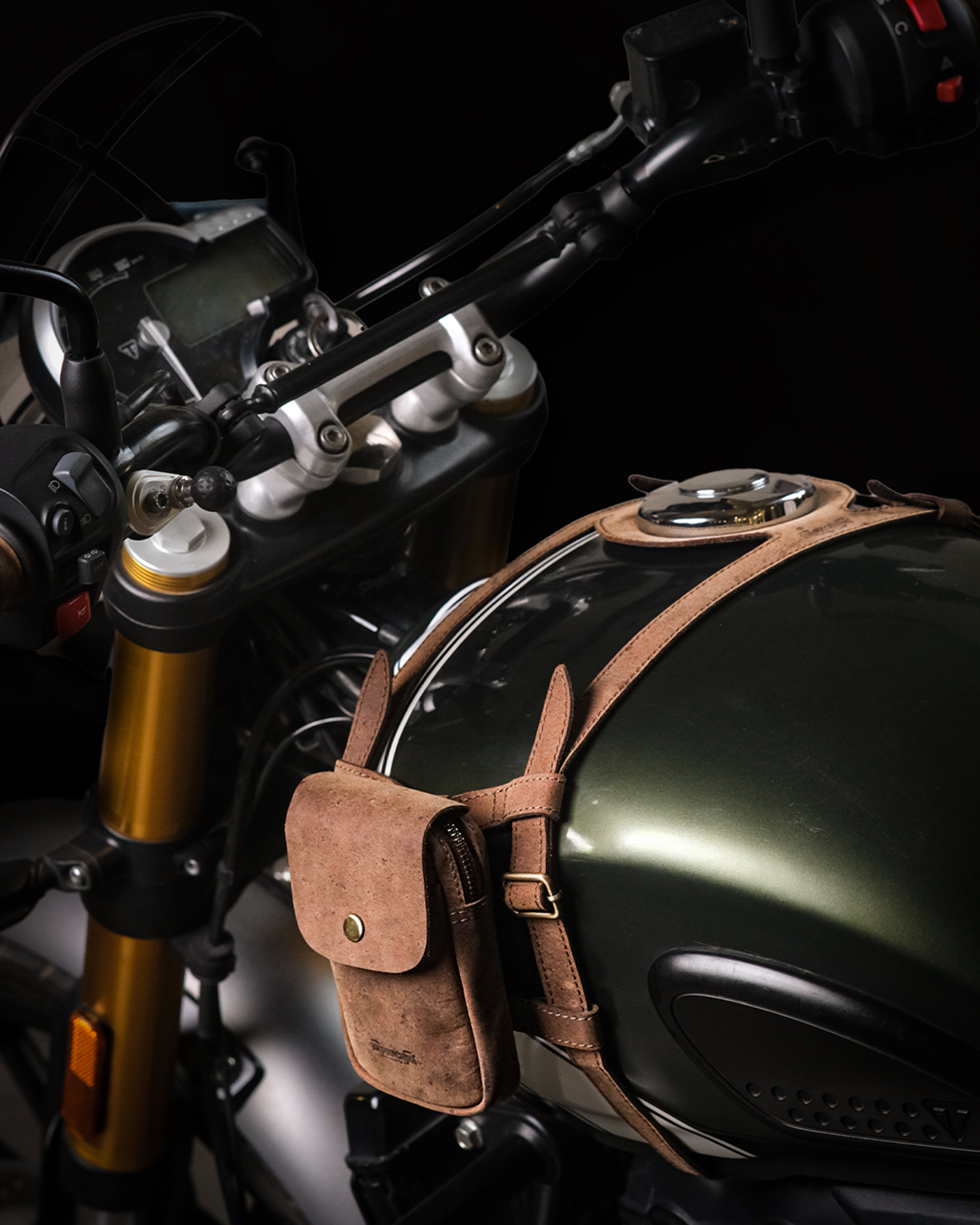 Close-up of a motorcycle with a brown leather pouch with tank strap attached to the fuel tank.