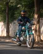 Man riding a teal motorcycle on a tree-lined street
