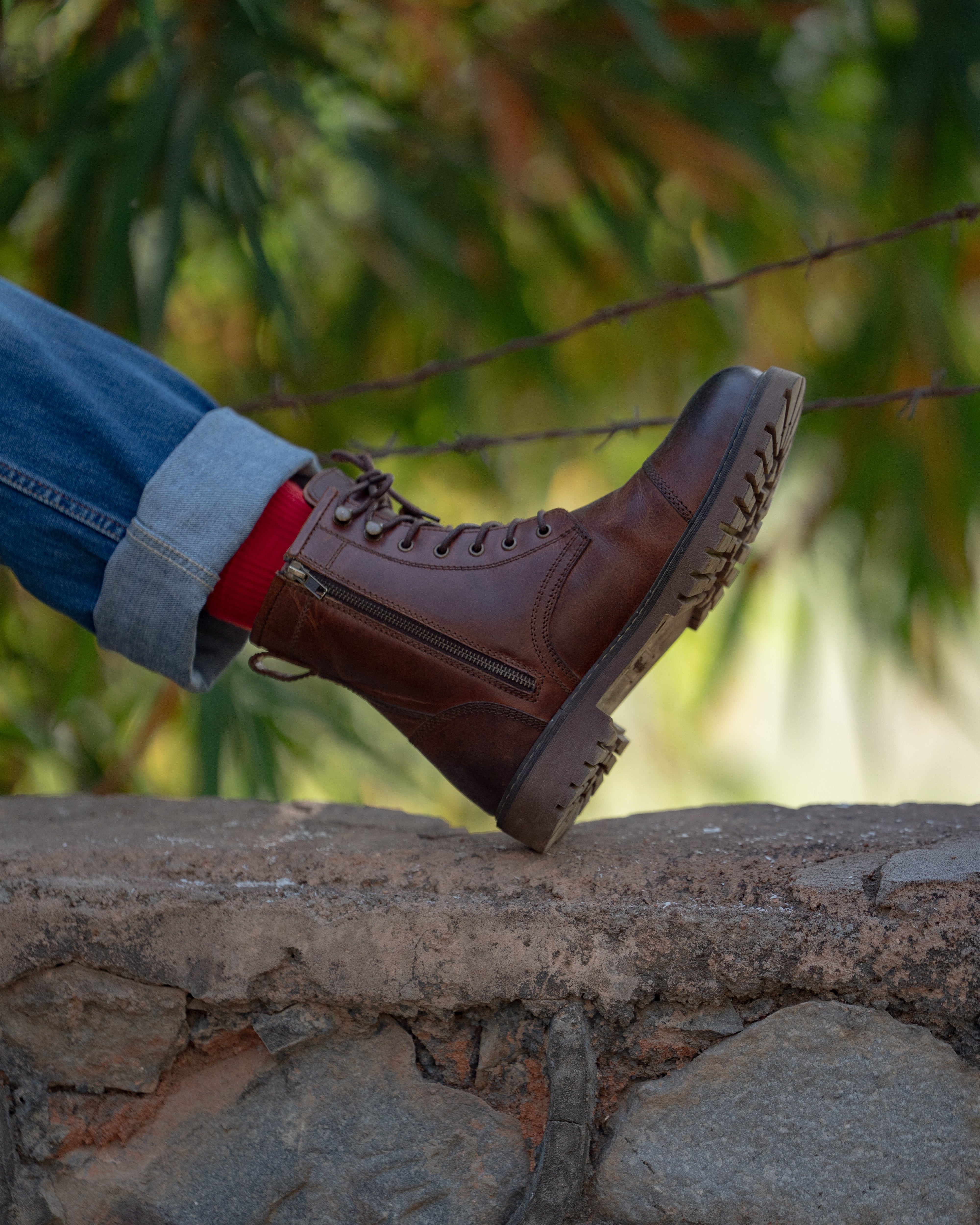 Brown leather boot on a stone wall with blurred greenery in the background