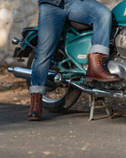 Person wearing brown boots and blue jeans sitting on a green motorcycle.