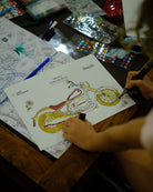Person coloring a motorcycle on a coloring book with various art supplies on a table.