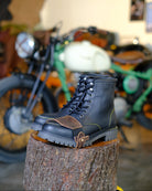 Black leather boot with mocha shoe protector on a tree stump with a motorcycle in the background