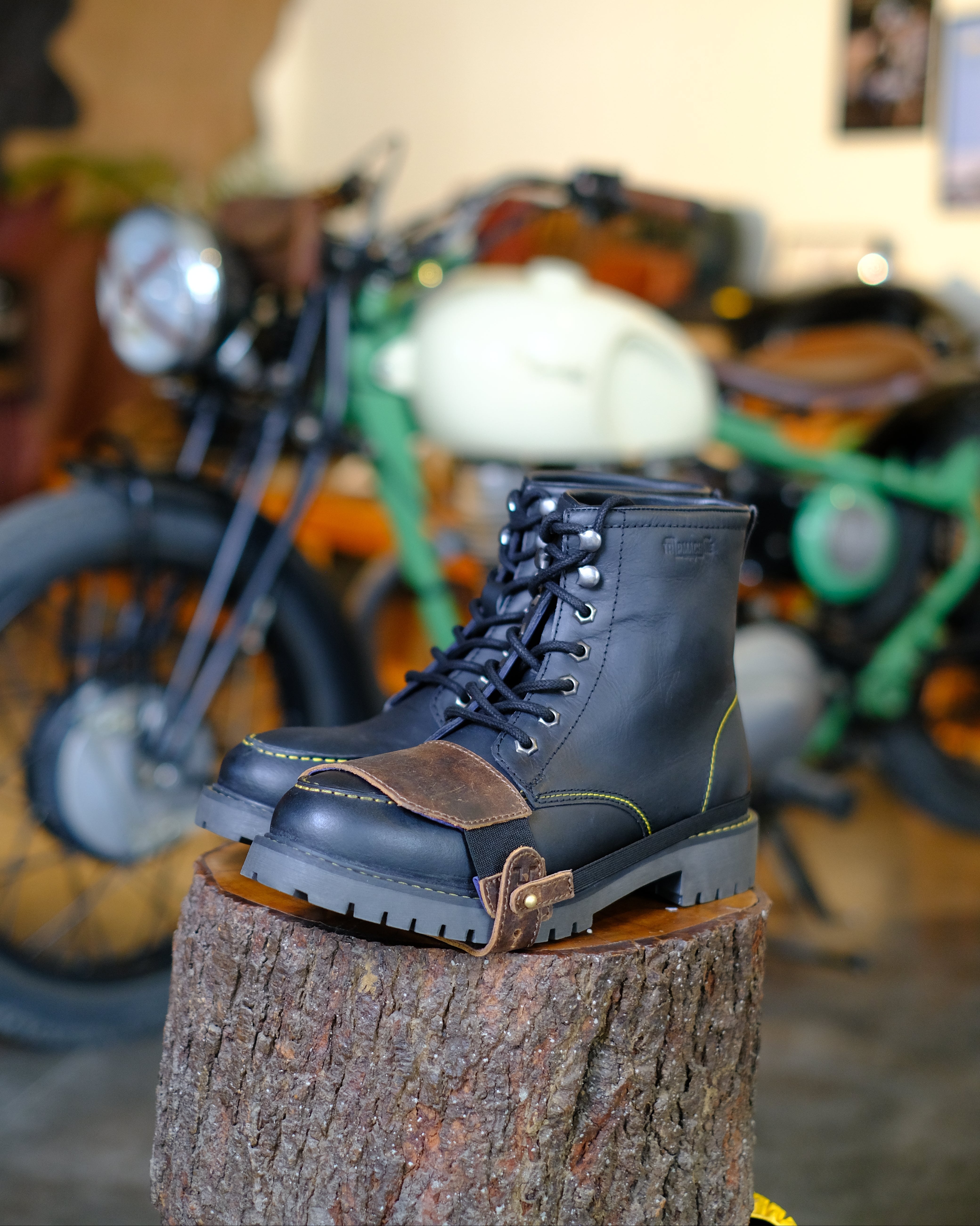 Black leather boot with mocha shoe protector on a tree stump with a motorcycle in the background