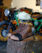 Brown leather boots with black shoe protector on a tree stump with motorcycles in the background