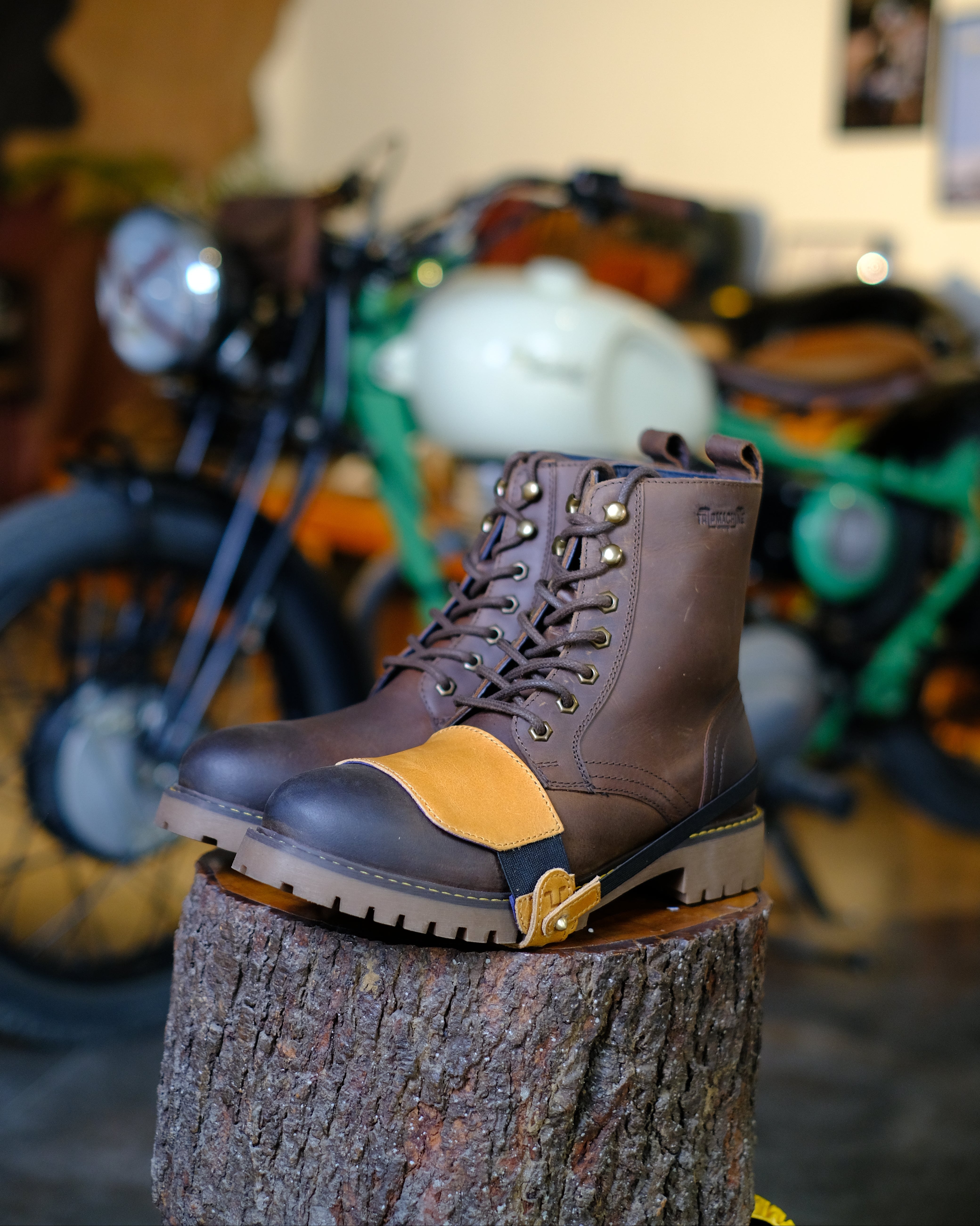 Brown leather boot with tan shoe protector on a tree stump in a motorcycle-themed room.
