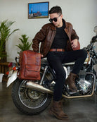 A man is seated on motorcycle with handmade genuine leather cherry red  color eastwood backpack mounted on a bike