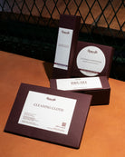 Set of leather care products including a cloth, brush, and conditioner on a brown surface.