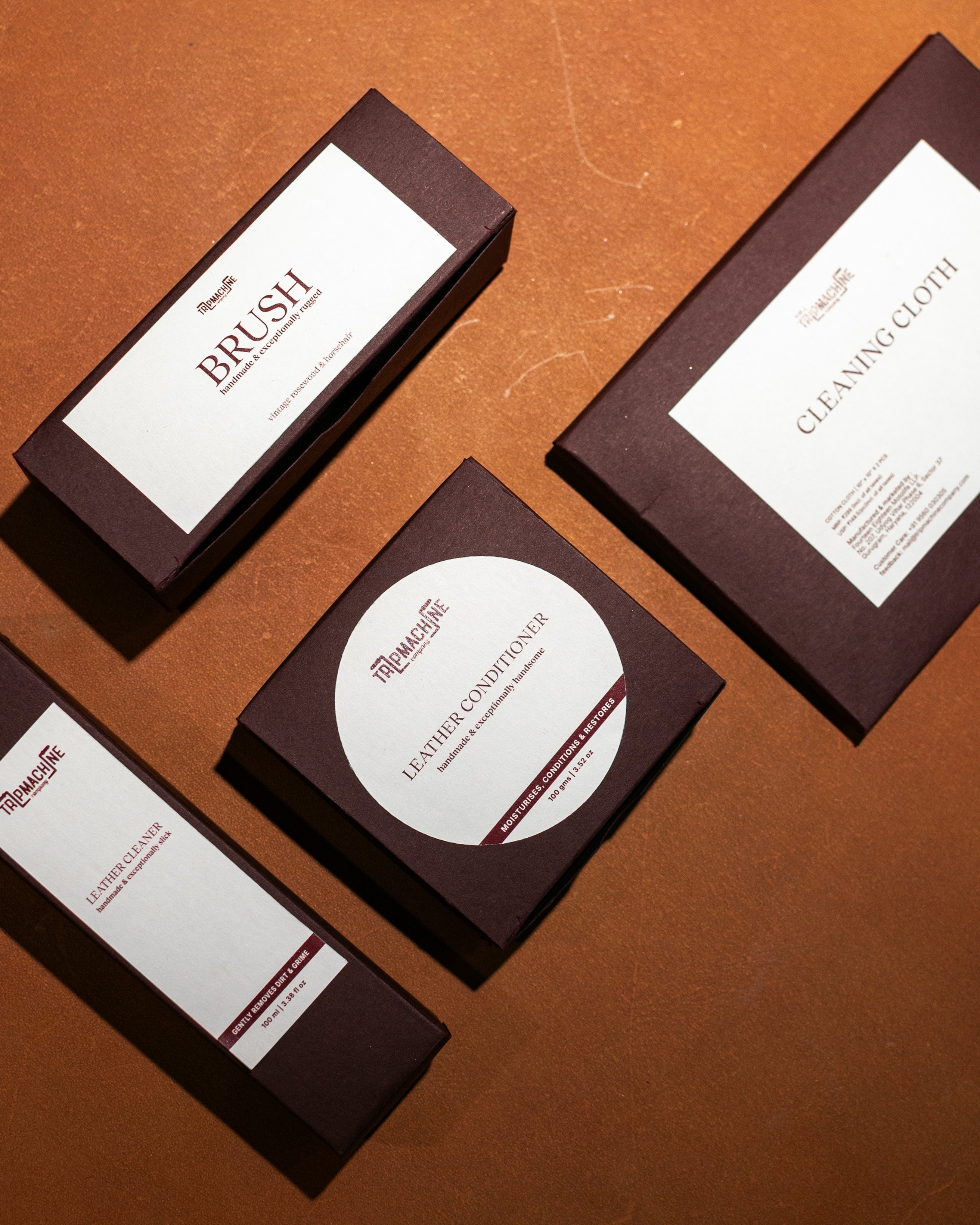 Set of leather care products including a brush, cleaning cloth, and leather conditioner on a brown surface.