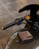 A brown leather bifold wallet with a chain strap detail, resting on a motorcycle tank next to a black chain.