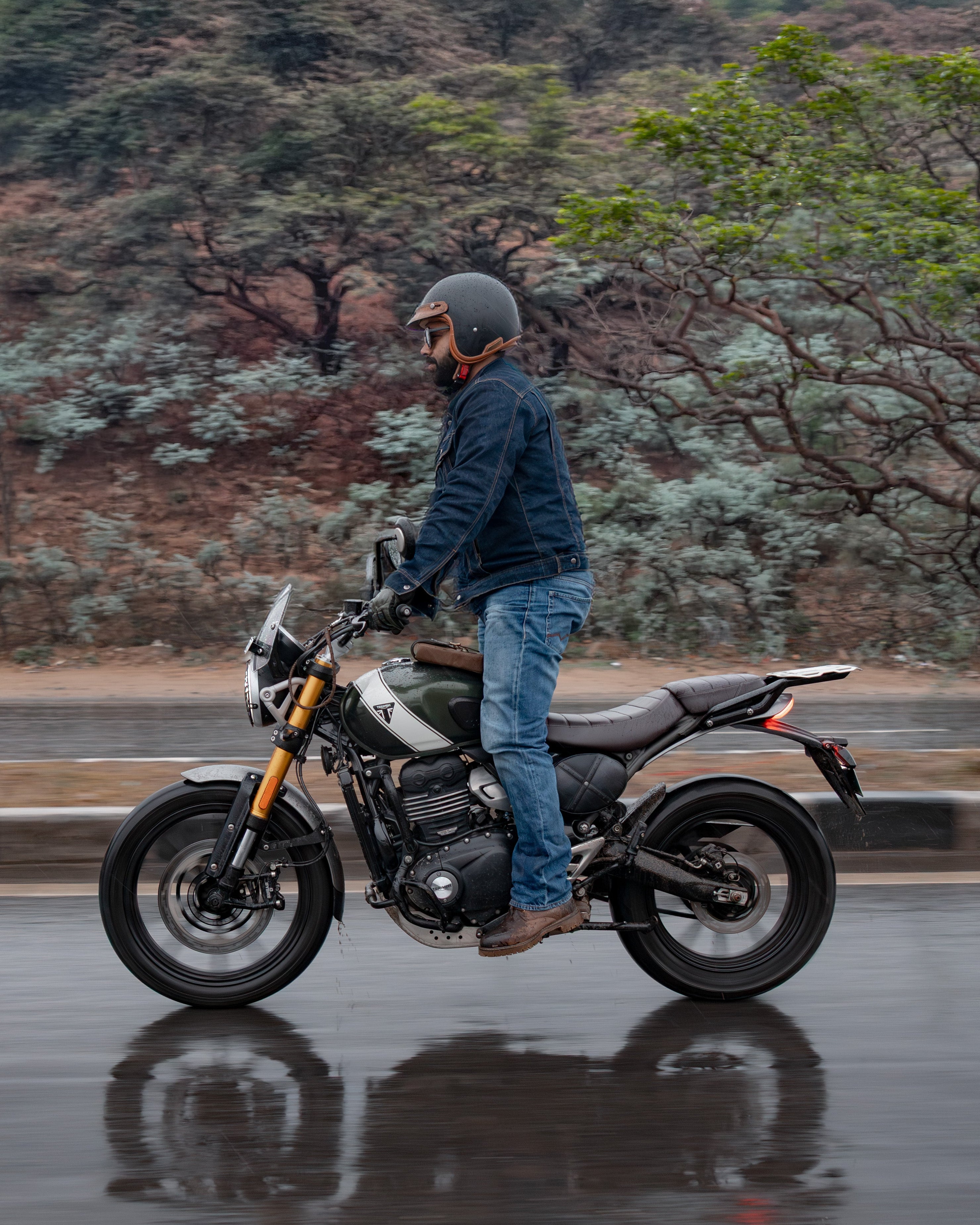 Person standing next to a motorcycle on a wet road with a forested background