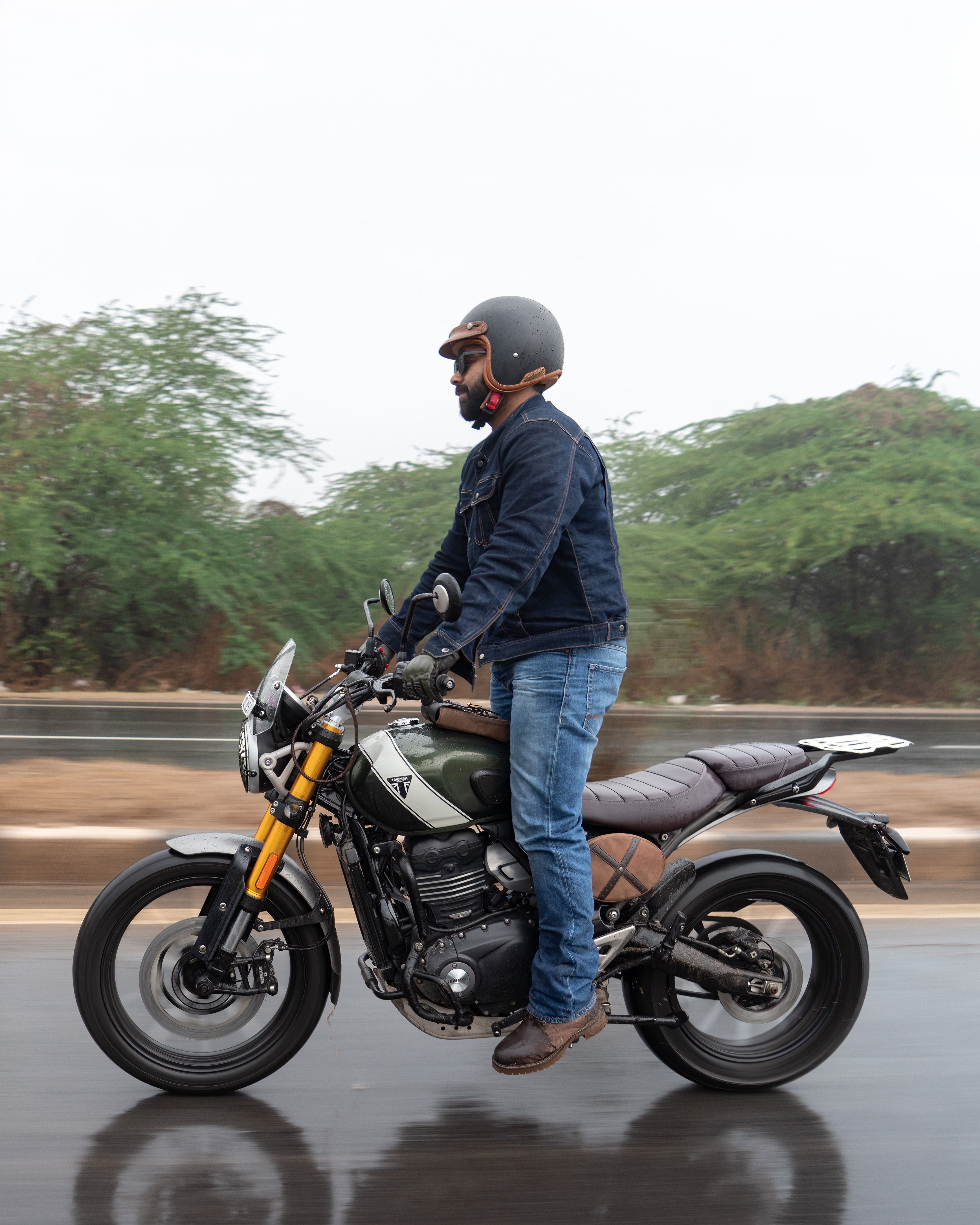 Man standing next to a motorcycle on a road with trees in the background