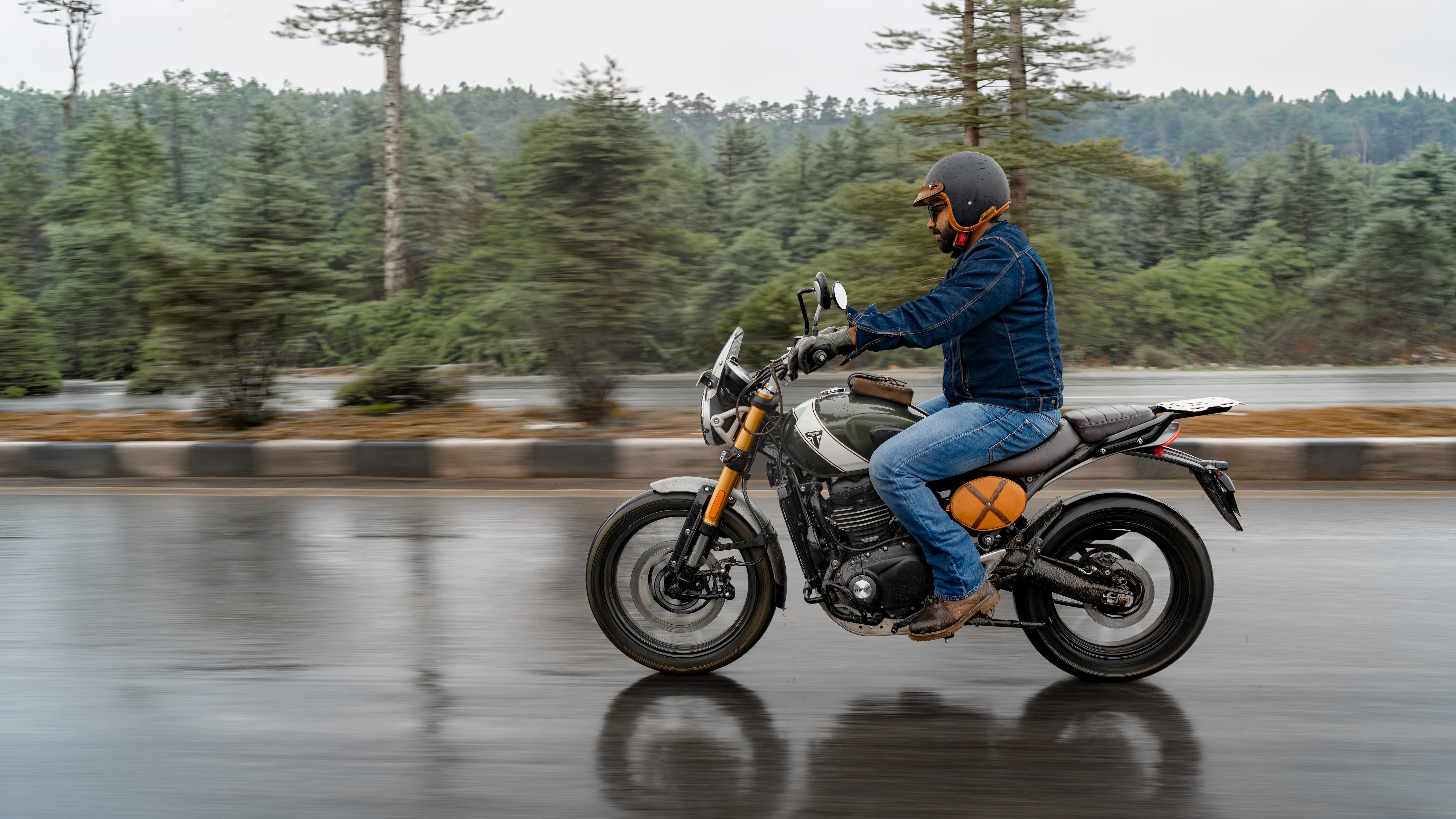 Person riding a motorcycle on a wet road with trees in the background
