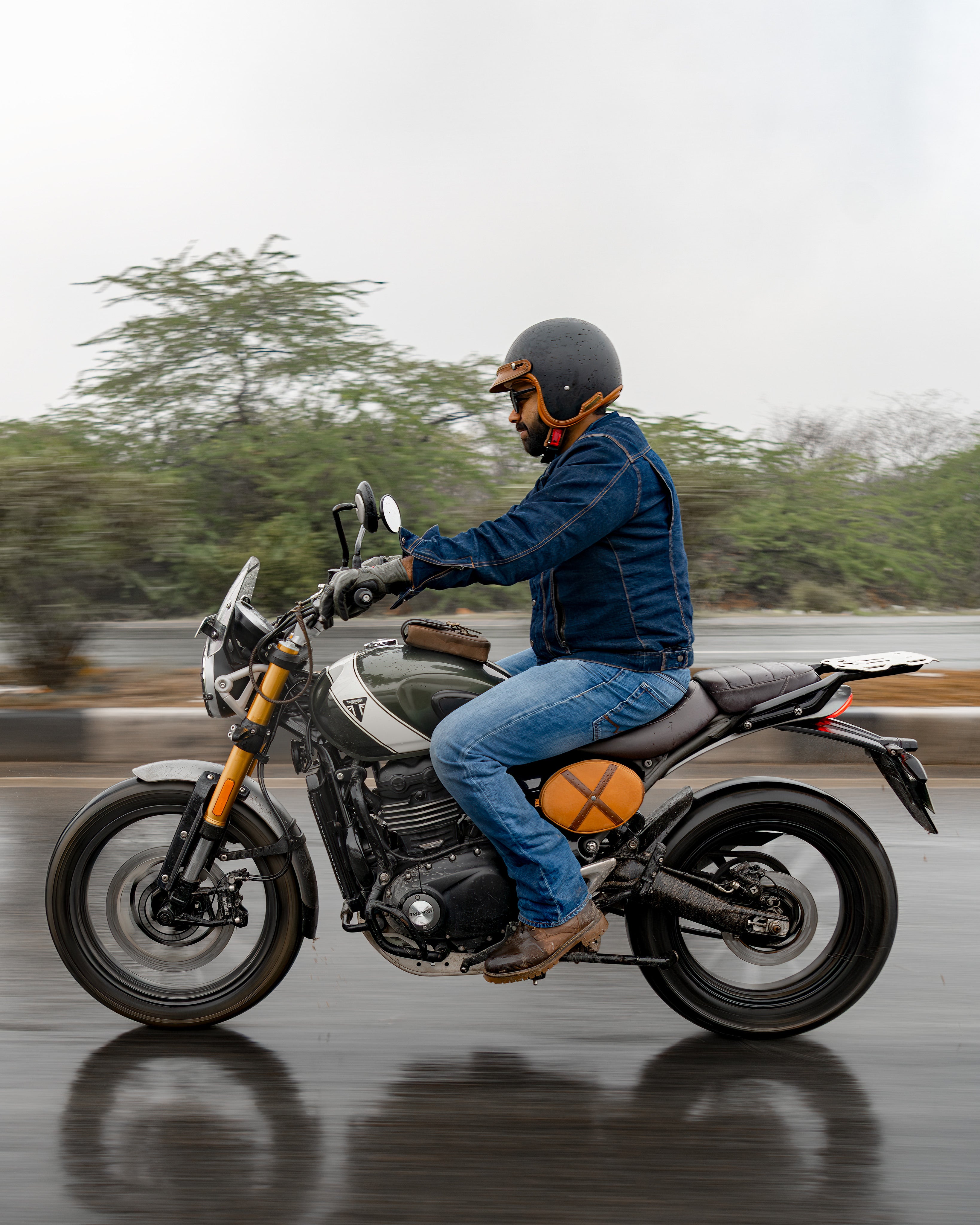Person riding a motorcycle on a wet road with trees in the background