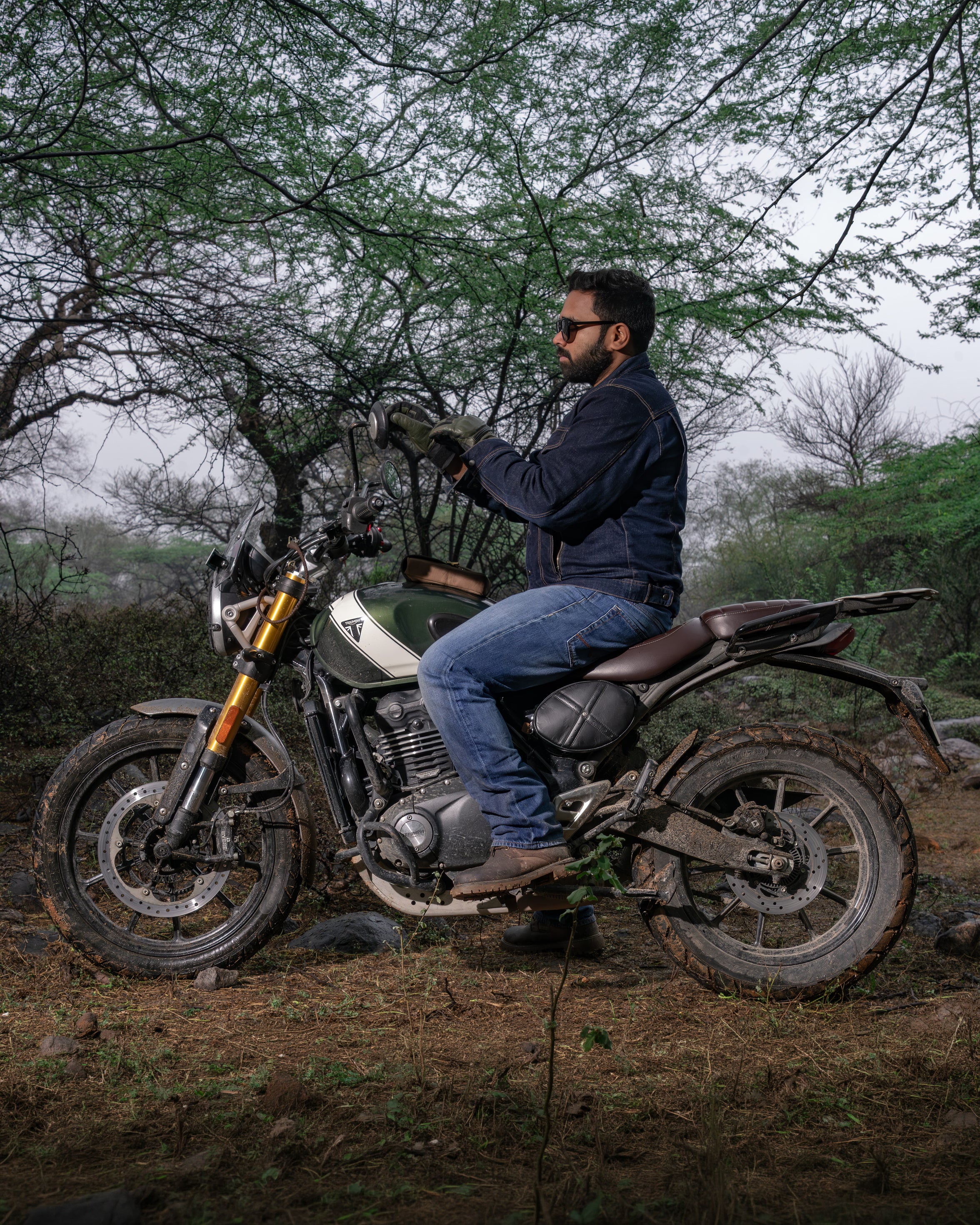 Man sitting on a motorcycle in a natural setting with trees and grass.