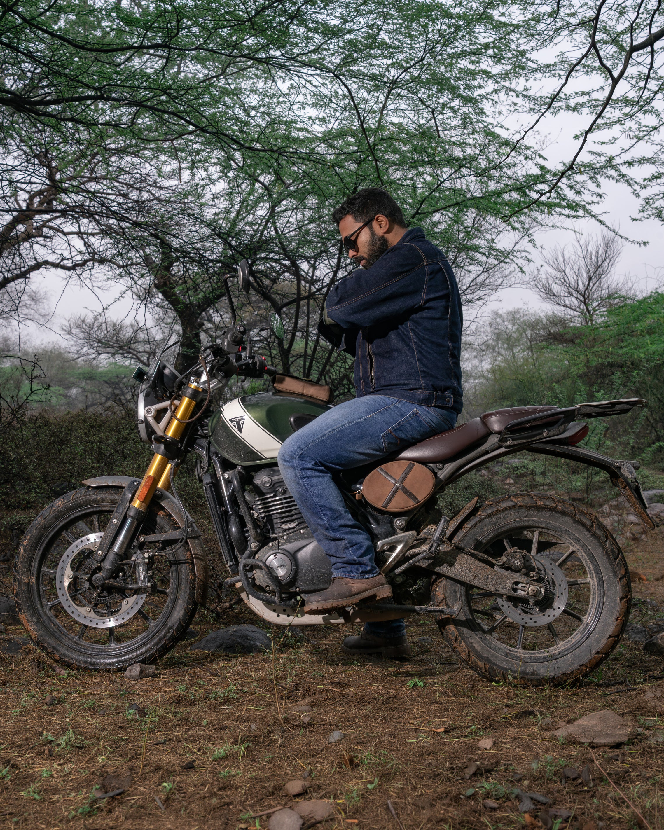 Person sitting on a motorcycle in a natural setting with trees and grass.