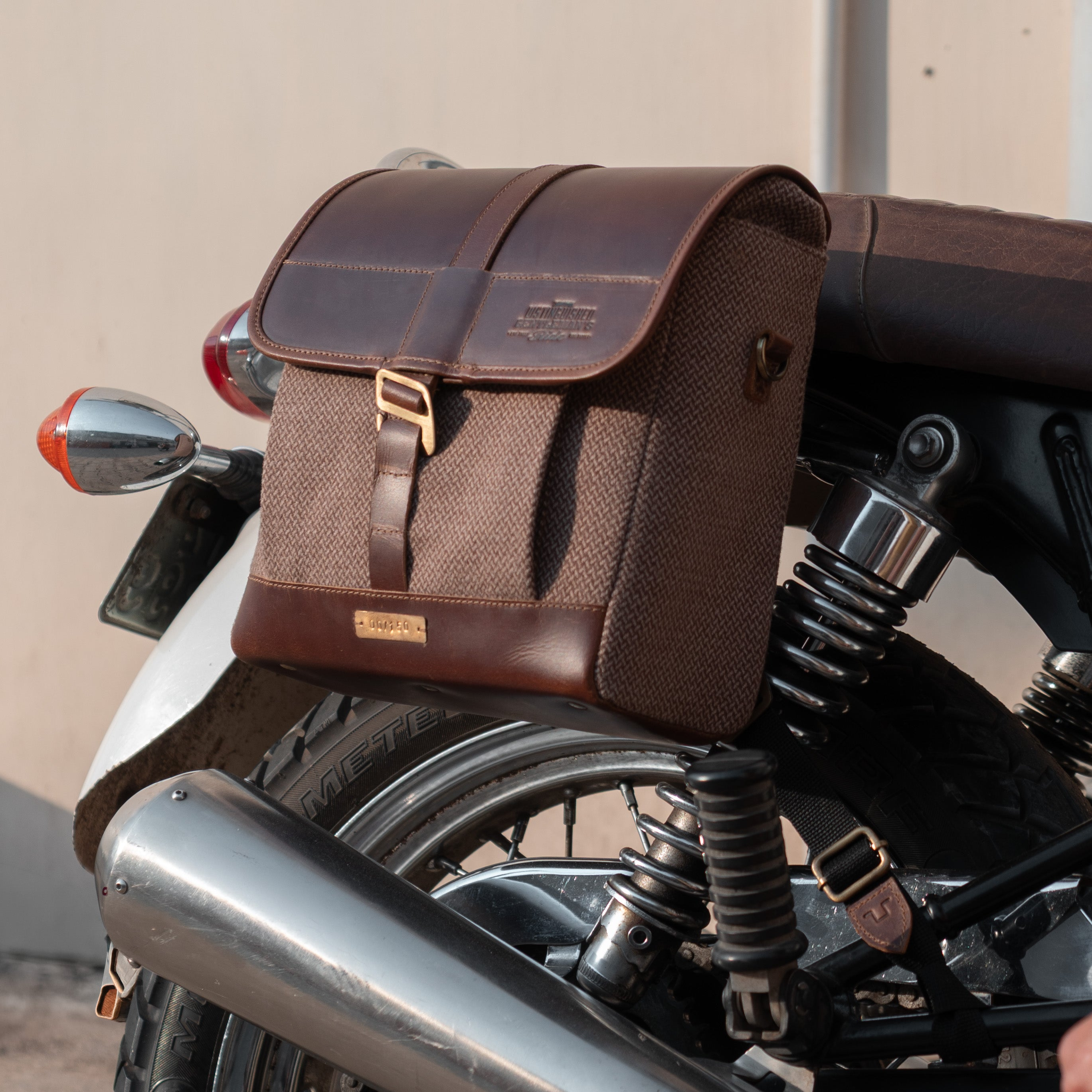 Brown leather bag on a motorcycle with a person's hand on the seat.