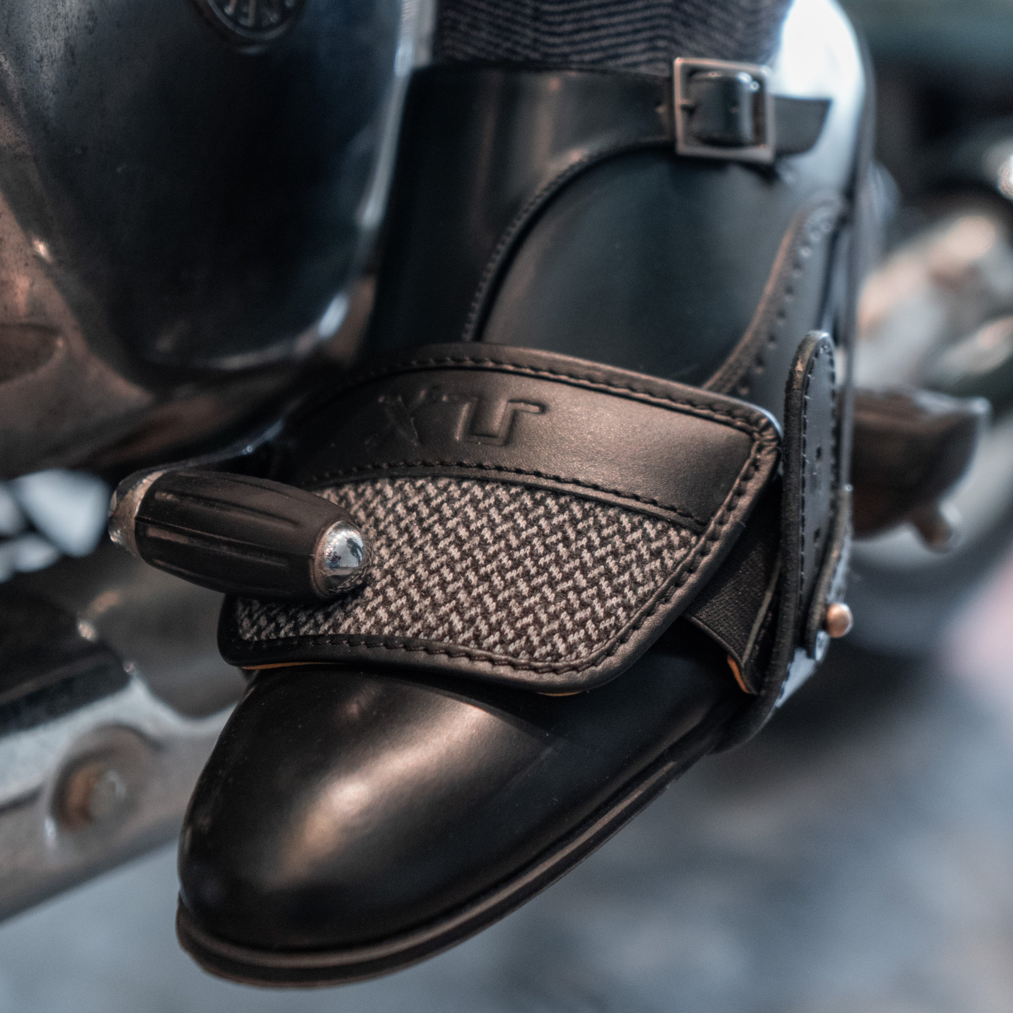 Close-up of a black leather boot with a textured strap and buckle, worn by a person.