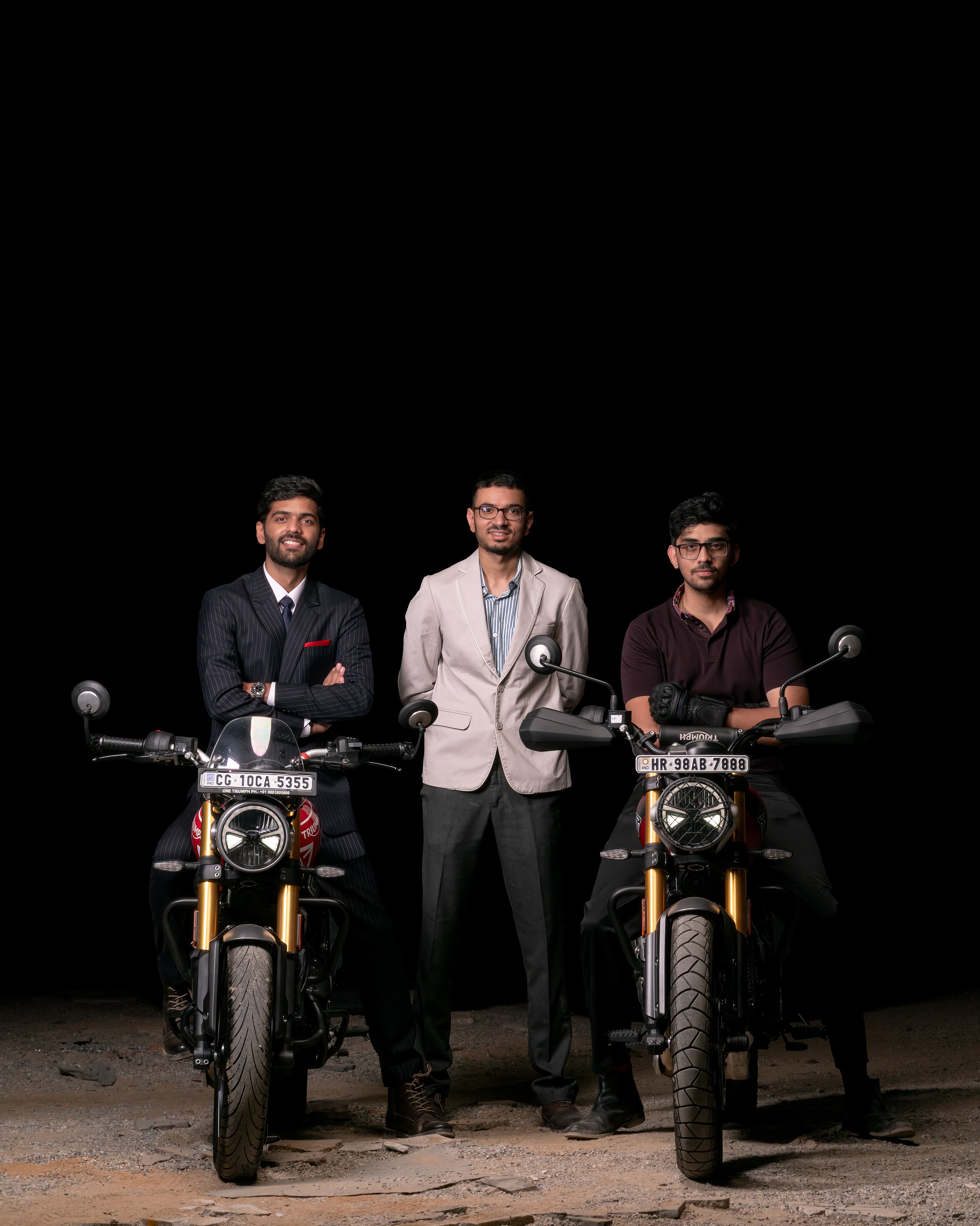 Three men standing between two motorcycles on a dark background